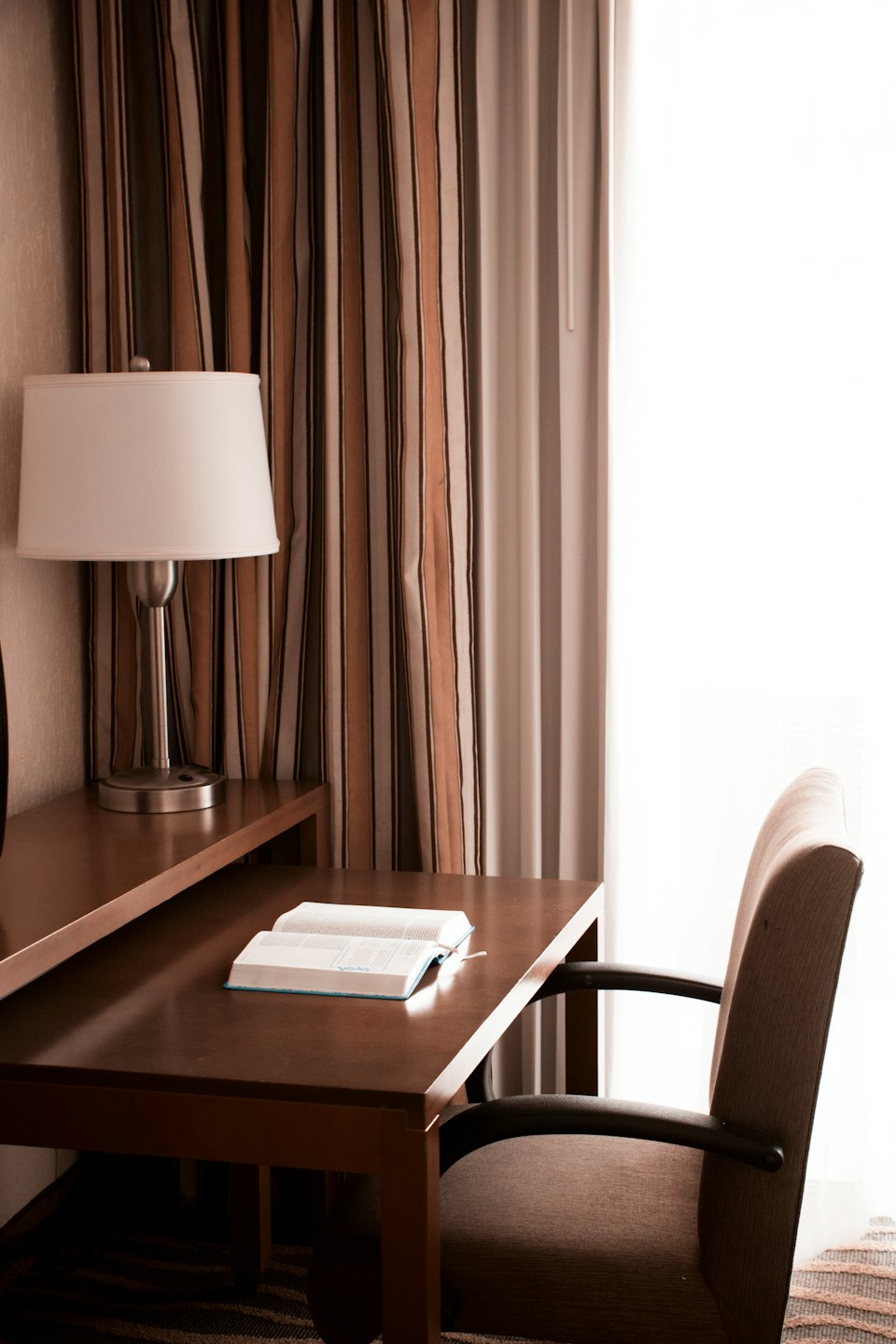 An open book sits on a wooden desk near a lamp.