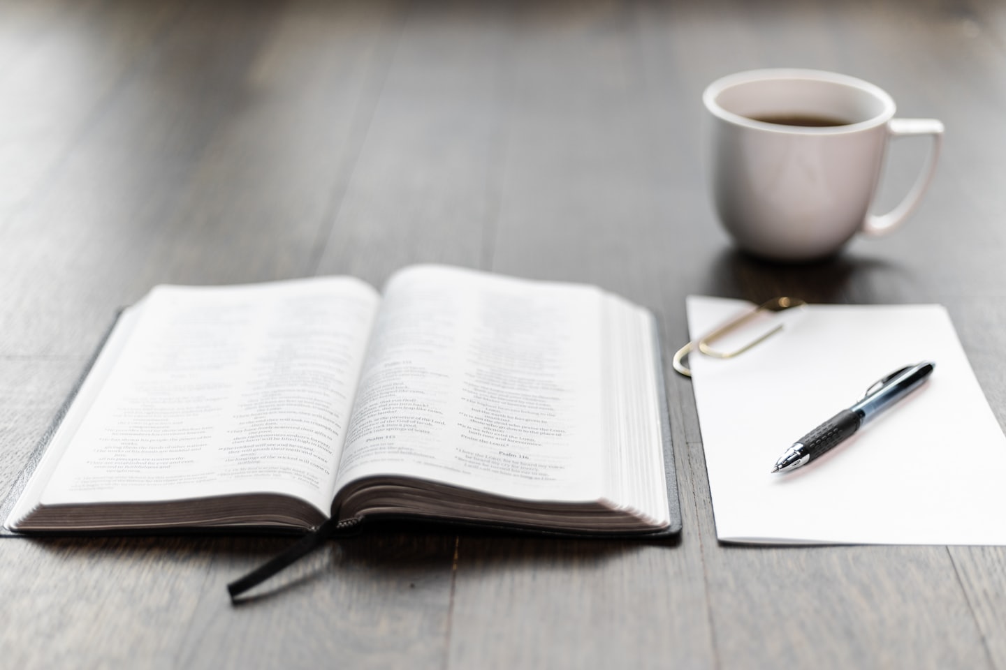 Open book, blank paper, pen, and coffee on a desk.