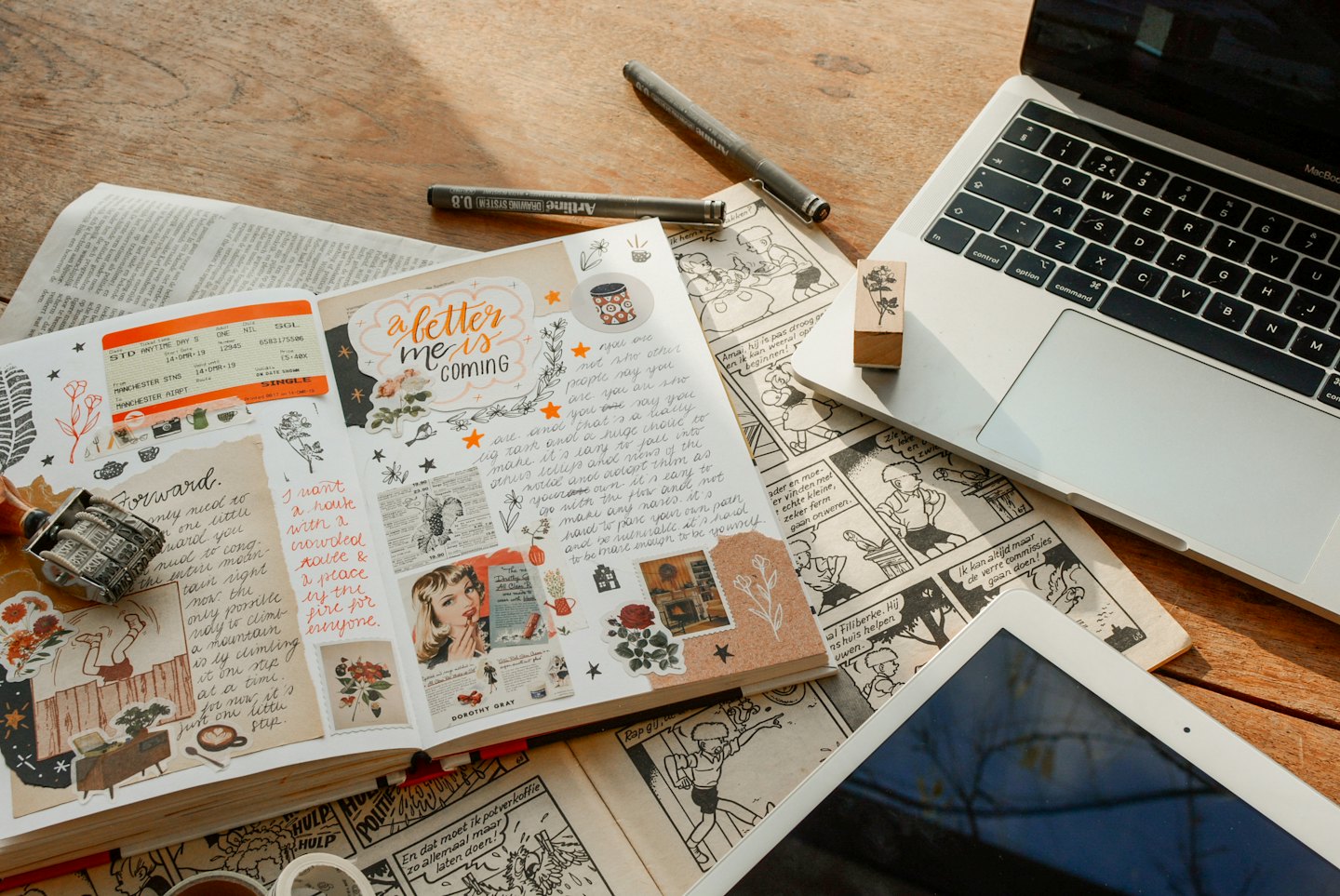 An open journal sits on a desk with a laptop and tablet.